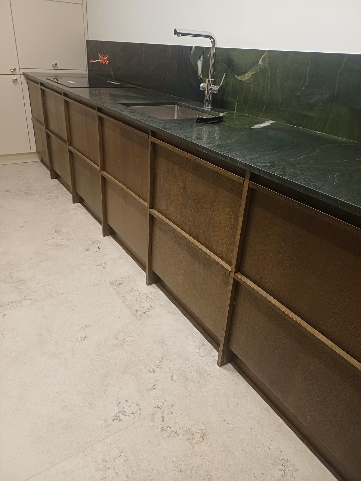 Dolne szafki kuchenne z ciemnymi frontami w ramach w kolorze drewna i zielonym blatem