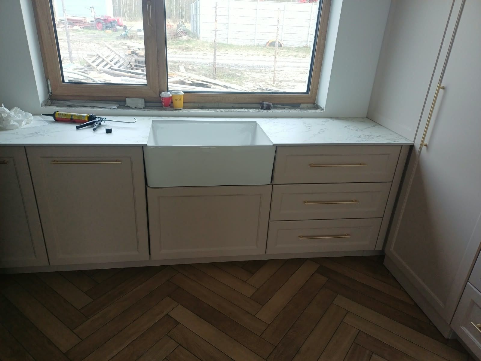 Ciąg szafek z frezowanymi frontami pod oknem, podłoga w jodełkę